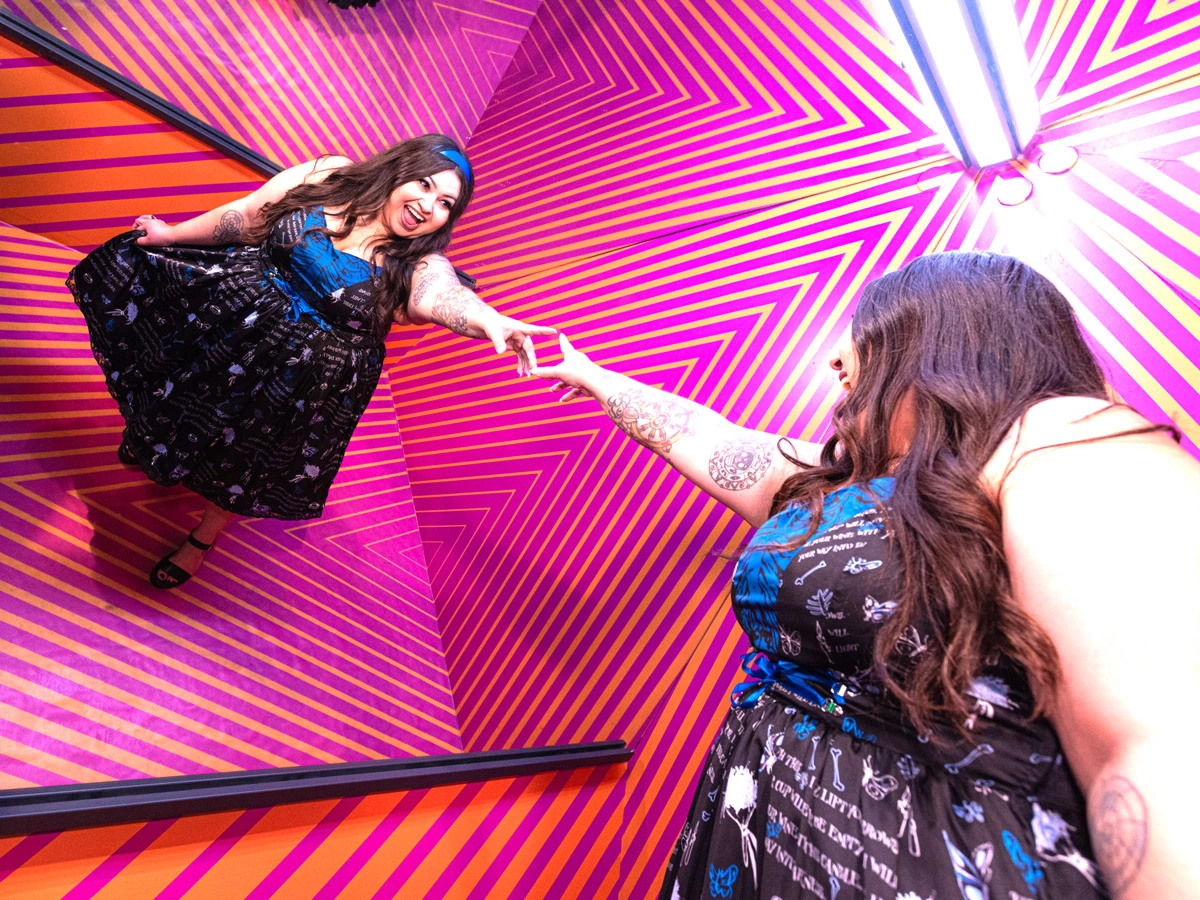 A woman is reaching out towards her reflection in the colorful Clone Room at Museum of Illusions Las Vegas.