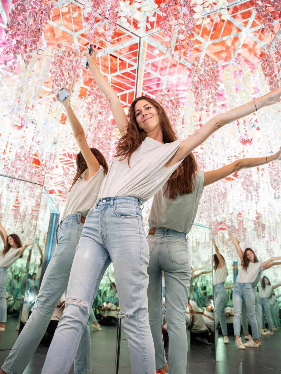 A young woman spreads her hands out in Museum of Illusions Las Vegas Infinity Room. Her infinite reflections are seen in the wall mirrors and glittery cascades hanging from the ceiling.