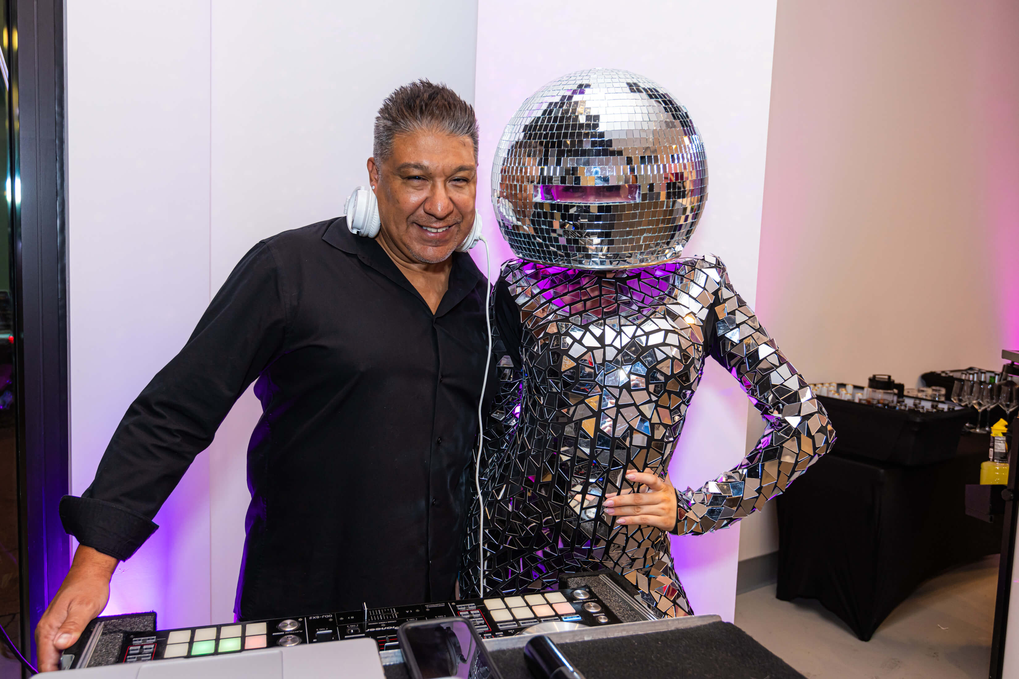 A person dressed in a glittery costume with a disco ball over their head is posing for a photo with a DJ at an event in Museum of Illusions Las Vegas.